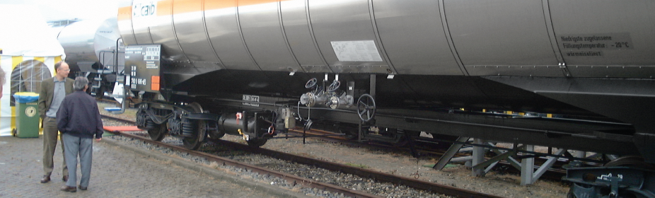 People standing next to an EMCO Wheaton G1600 automatic train refueling system on display at an exhibition.